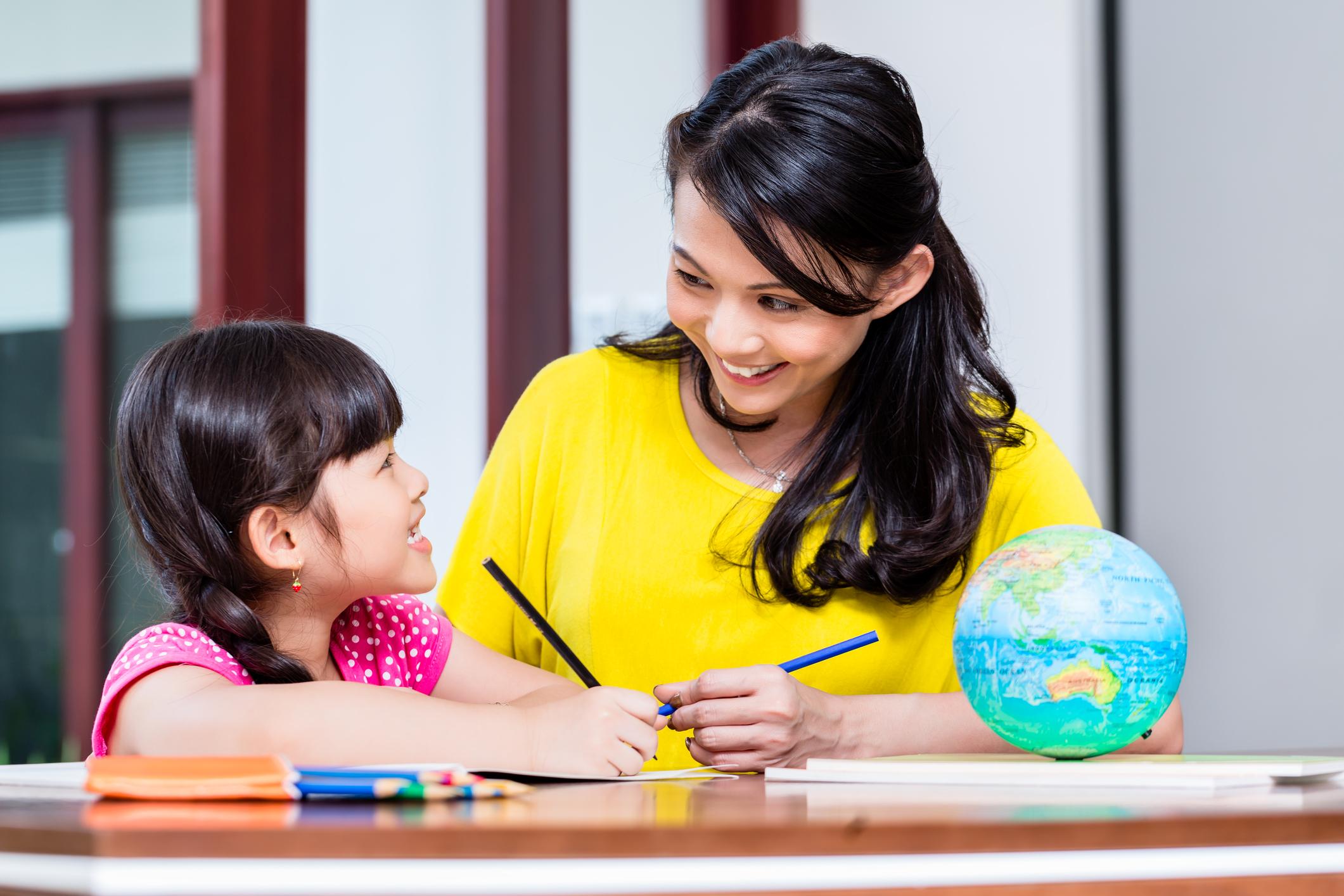 Mother teaching child at home with a globe and colored pencils